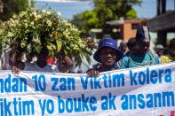 Cholera survivors carry the Creole message: "10 years, victims of cholera are tired" as they march to the former UN base in Mirebalais, Haiti, Monday, Oct. 19, 2020. Ten years after a cholera epidemic swept through Haiti and killed thousands, families of victims still struggle financially and await compensation from the United Nations as many continue to drink from and bathe in a river that became ground zero for the waterborne disease. (AP Photo/Dieu Nalio Chery)