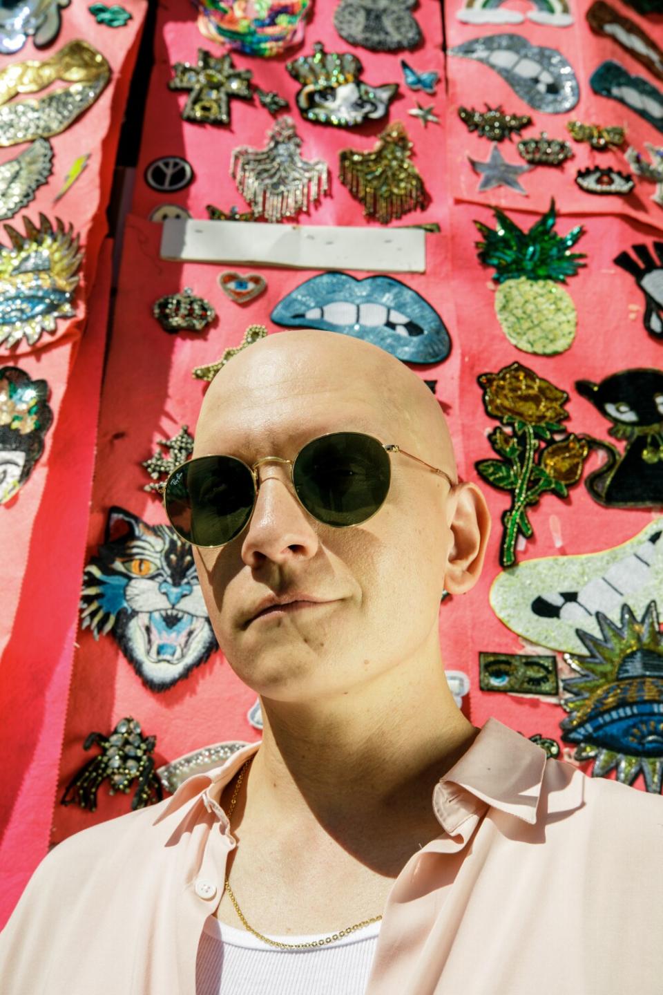 A man in sunglasses poses for a portrait in front of a stall selling patches.