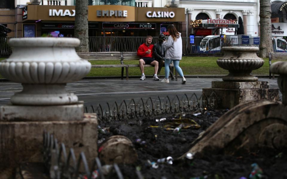 Tourists post for photos with a statue in view of rubbish left by football fans in Leicester Square on June 19, 2021 in London, England. - GETTY IMAGES