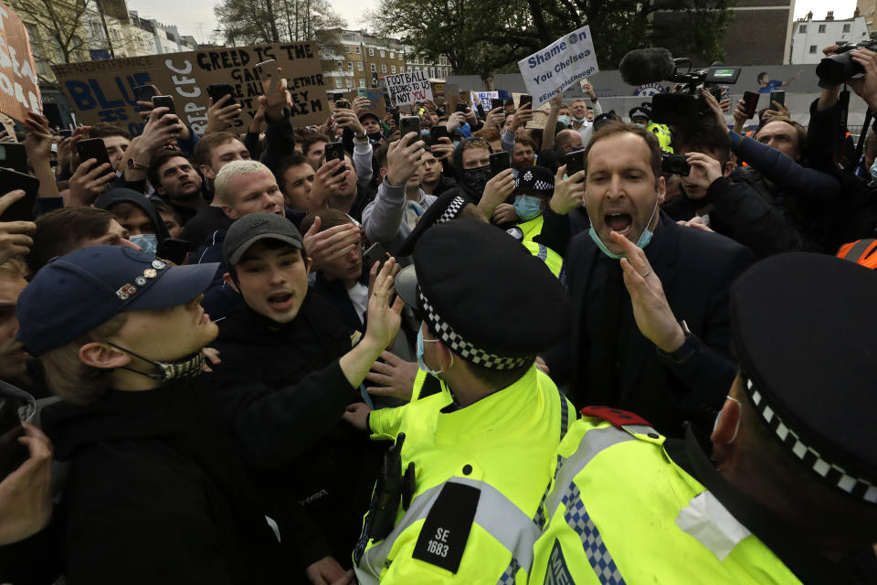 El exarquero del Chelsea, Petr Cech (derecha), detrás de un grupo de policías, trata de calmar a hinchas que protestan en Londres contra la creación de la Superliga europea, el martes 20 de abril de 2021 (AP Foto/Matt Dunham)