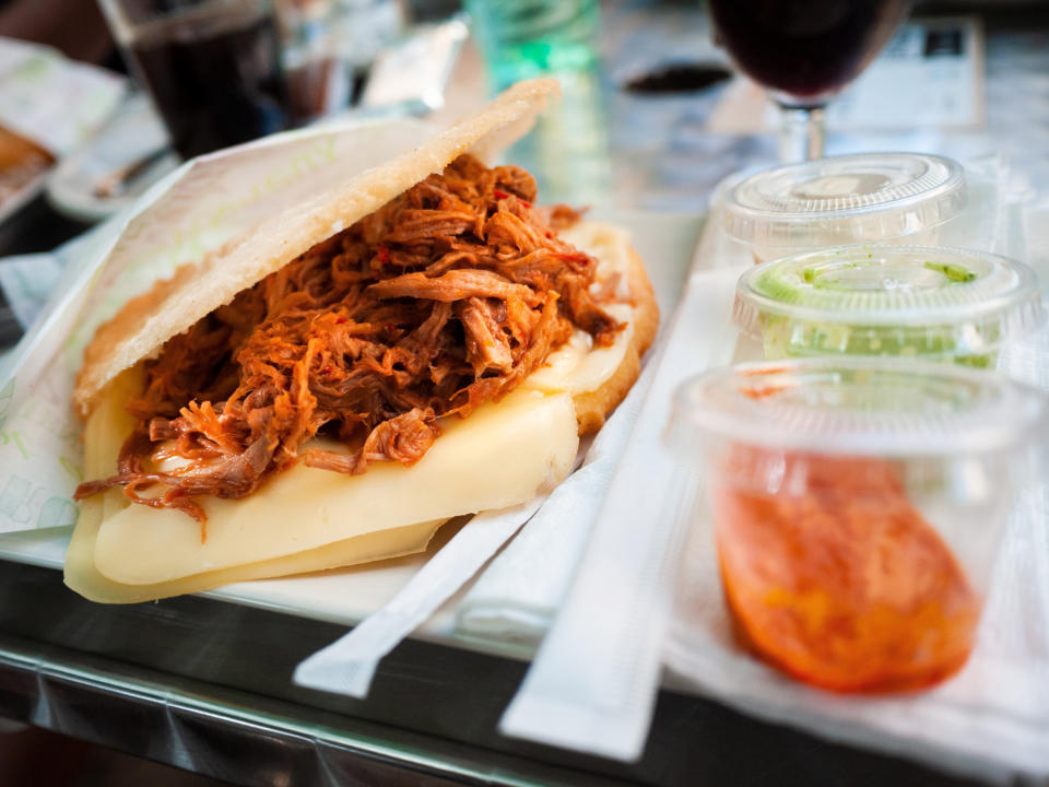 Arepa filled with cheese and shredded meat on a plate with sauces on the side