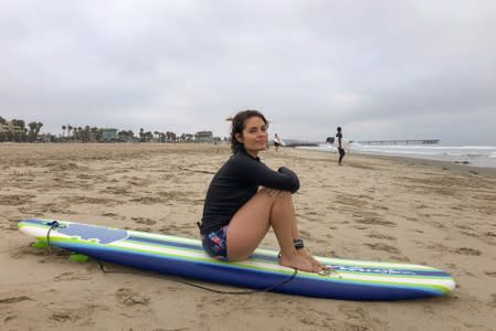 Beginner surfer Nicole Adams sits on her imported surfboard as she takes break from surfing on the beach in Venice, California