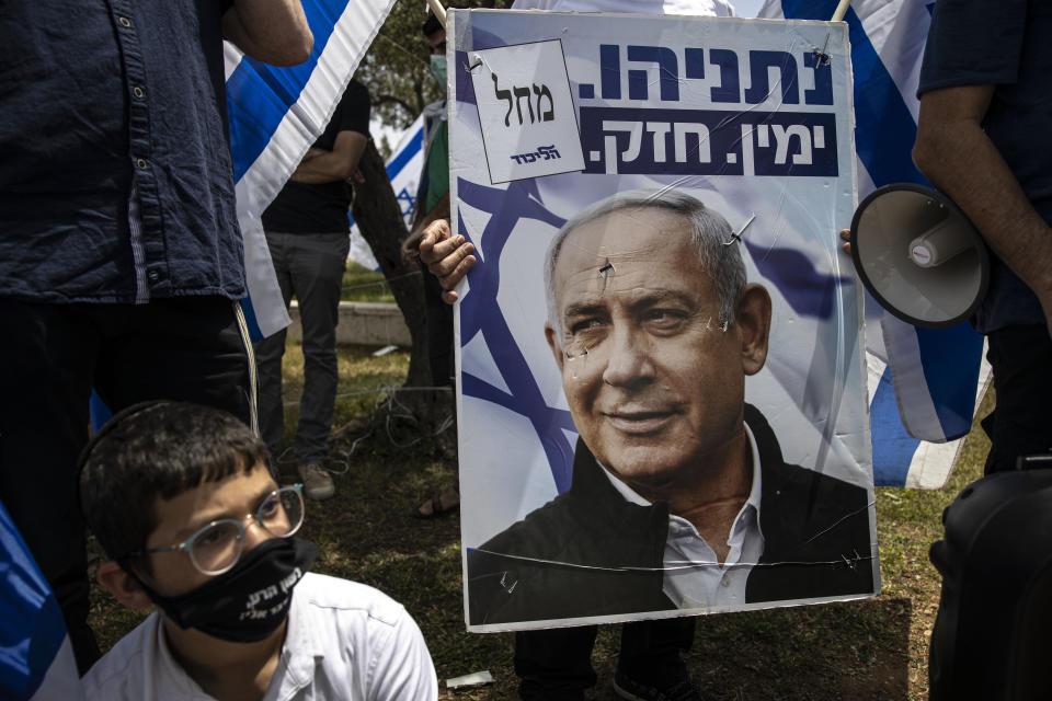 An Israeli protester wears a mask amid concerns over the country's coronavirus outbreak looks on a poster of Prime Minister Benjamin Netanyahu during a protest by supporters of Prime Minister Benjamin Netanyahu in front of Israel's Supreme Court in Jerusalem, Sunday, May 3, 2020. Israel's high court heard petitions Sunday that seek to block Prime Minister Benjamin Netanyahu from forming a government because he has been charged with serious crimes. (AP Photo/Tsafrir Abayov)