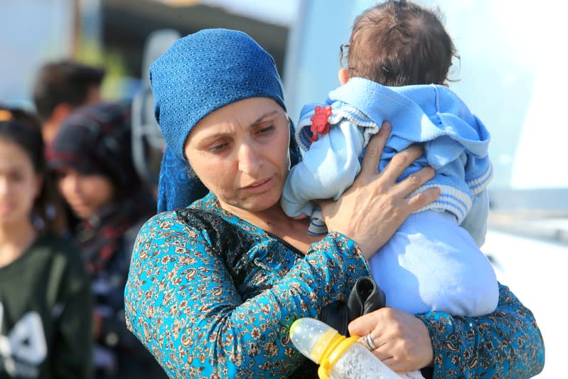 A displaced Syrian woman, who fled violence after the Turkish offensive in Syria, carries her baby upon arrival at a refugee camp in Bardarash on the outskirts of Dohuk