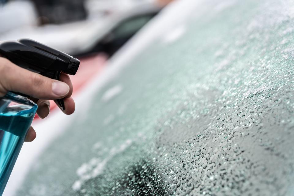 Man uses a bottle of de-icer to defrost the ice-covered windshield of his car.