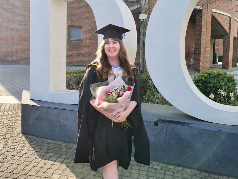 alexis in a cap and gown holding flowers at her graduation in ireland