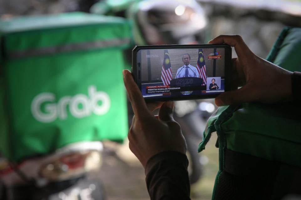 Food delivery rider watching the live telecast of Prime Minister Tan Sri Muhyiddin Yassin’s announcement of a movement control order extension due to the Covid-19 pandemic in Shah Alam April 10, 2020. — Picture by Yusof Mat Isa