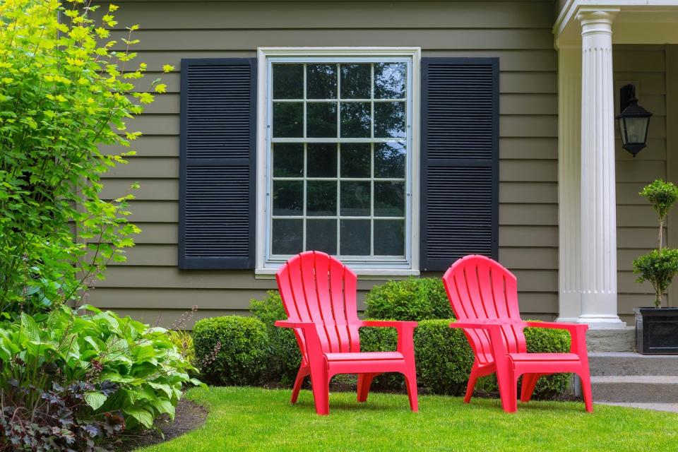 two red adirondack chairs in front law of grey house