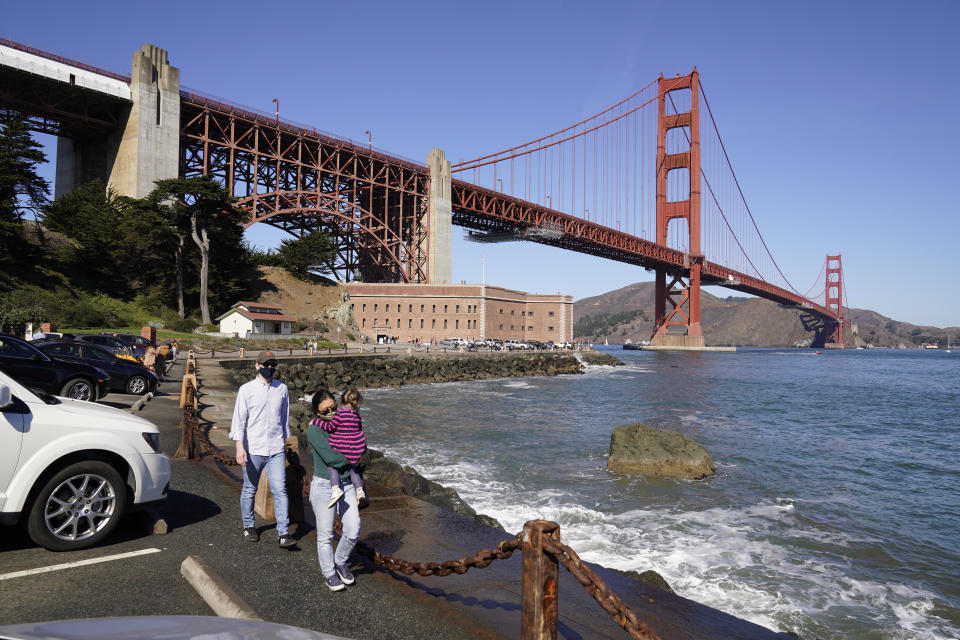 On a clear day people walk along a seawall with Fort Point and the Golden Gate Bridge in the background in San Francisco on Oct. 11, 2020. Wildfires that scorched huge swaths of the West Coast churned out massive plumes of choking smoke that blanketed millions of people with hazardous pollution that spiked emergency room visits and that experts say could continue generating health problems for years. An Associated Press analysis of air quality data shows 5.2 million people in five states were hit with hazardous levels of pollution for at least a day. (AP Photo/Eric Risberg)