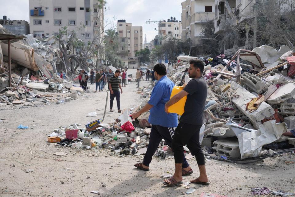 A Palestinian carries a water canister by the buildings destroyed in an Israeli airstrike in Nuseirat camp in the central Gaza Strip, Monday, Oct. 16, 2023.