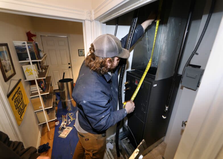 John Paul uses a tape measure during the installation of a heat pump in an 80-year-old rowhouse Friday, Jan. 20, 2023, in northwest Denver. (AP Photo/David Zalubowski)