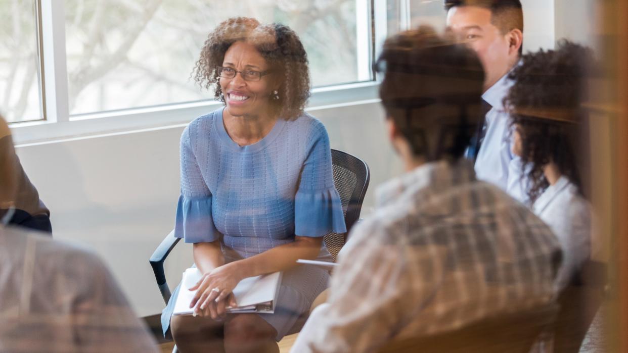 Cheerful mature African American manager smiles while listening to a colleague during a weekly staff meeting.