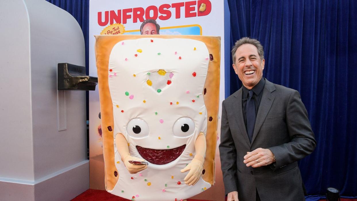 jerry seinfeld smiling as he stands next to a pop tart mascot at the premiere of his film unfrosted