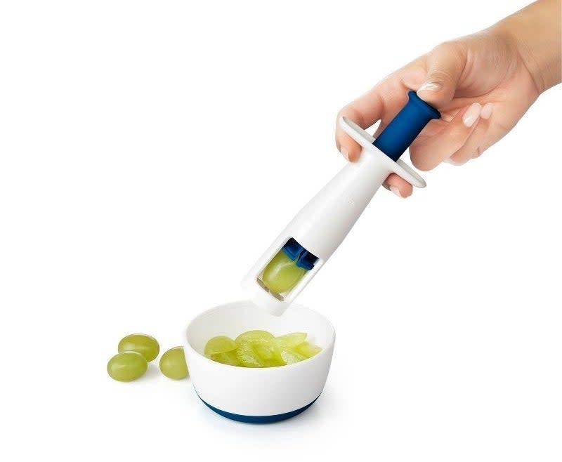 Hand using a grape cutter to slice grapes into a bowl