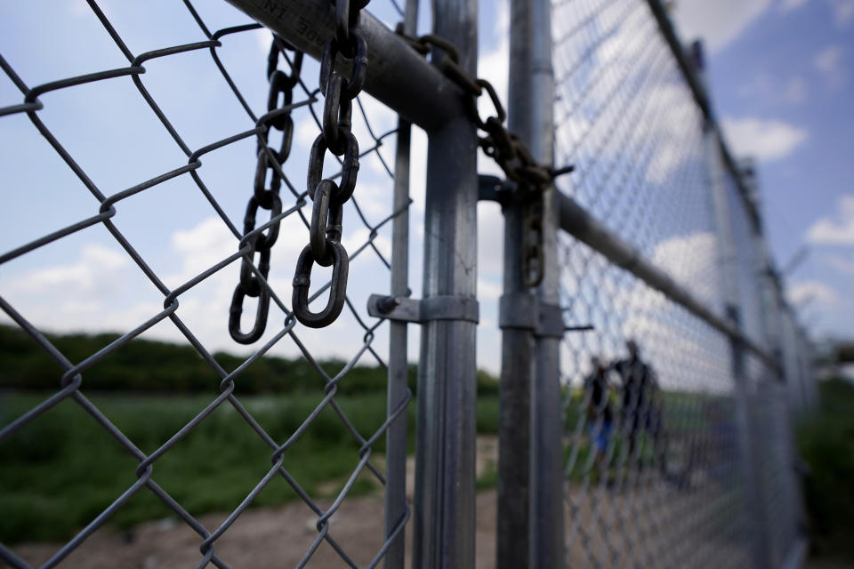 Migrants who crossed the Rio Grande illegally, stand behind an unlocked gate at Heavenly Farms, a pecan farm, Heavenly Farms, owned by Hugo and Magali Urbina, Friday, Aug. 26, 2022, in Eagle Pass, Texas. The Texas National Guard and state troopers built a fence around Heavenly Farms and, in mid-August, locked a gate to arrest migrants after crossing the Rio Grande illegally. The Border Patrol felt the lock impeded operations and had it removed. (AP Photo/Eric Gay)