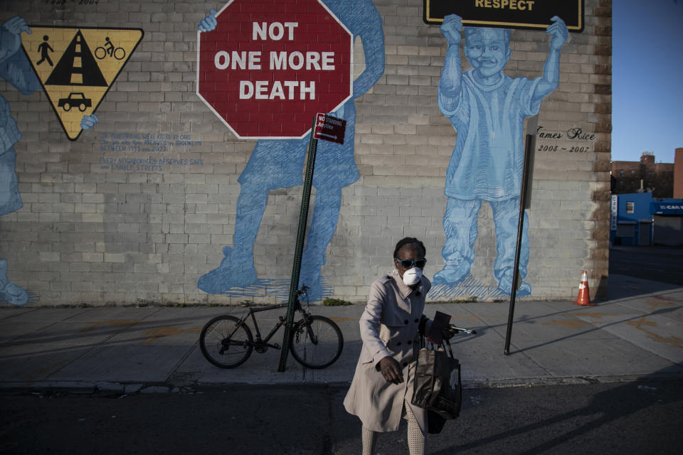 A woman wearing a mask crosses the street in front of a mural about traffic accidents reading, "NOT ONE MORE DEATH" in the Brooklyn borough of New York, March 27, 2020. (AP Photo/Wong Maye-E)