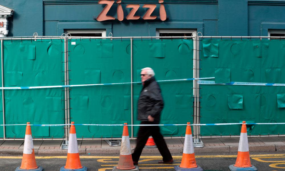 Man walks past green barricade in front of Zizzi restaurant in Salisbury