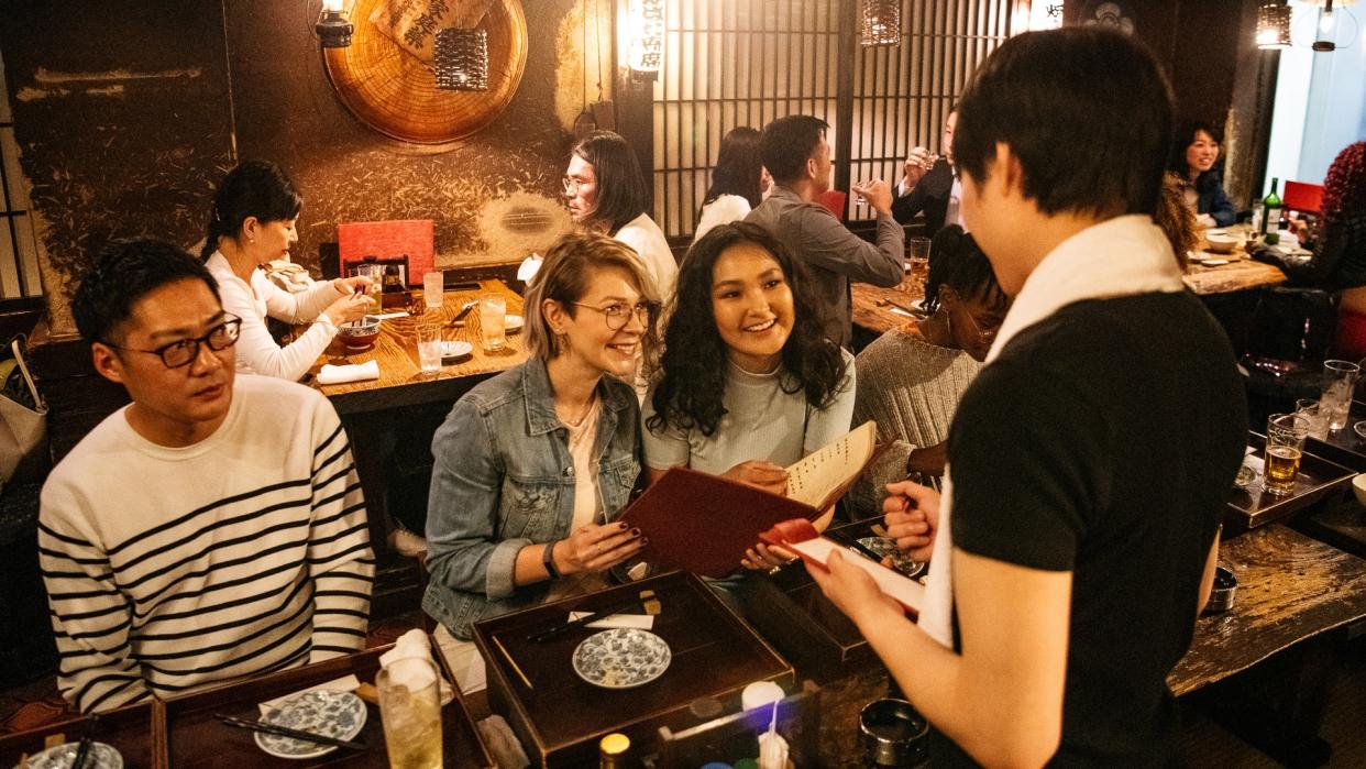 Young women ordering food in busy Japanese restaurant, fun, night out, flirting.