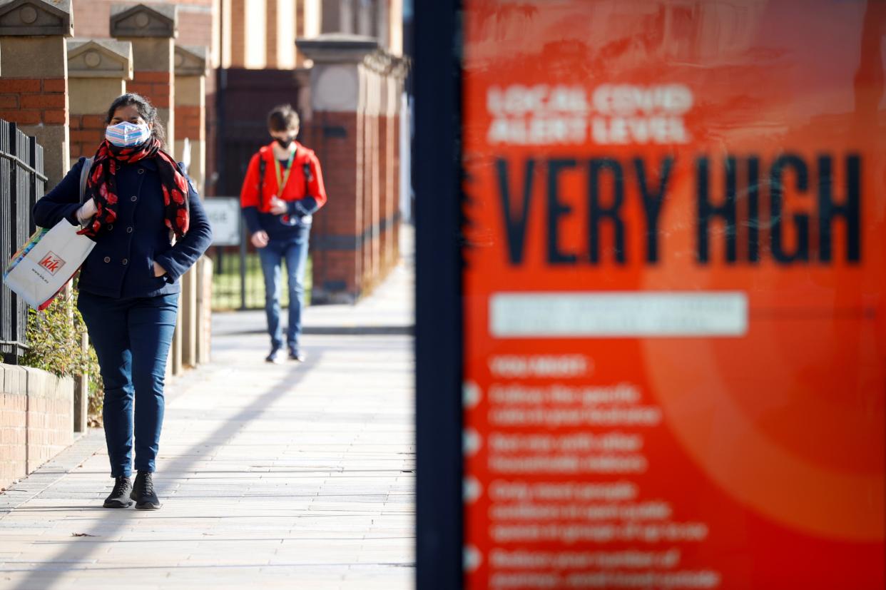 People wearing protective masks walk behind a Covid warning sign in Liverpool (Reuters)