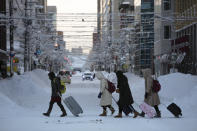 In this Feb. 6, 2020, photo, a group of tourists crosses an icy street with their luggage bags in Sapporo, Hokkaido, Japan. The Japanese island of Hokkaido is declaring a state of emergency over the rapid spread of the new virus there. (AP Photo/Jae C. Hong)