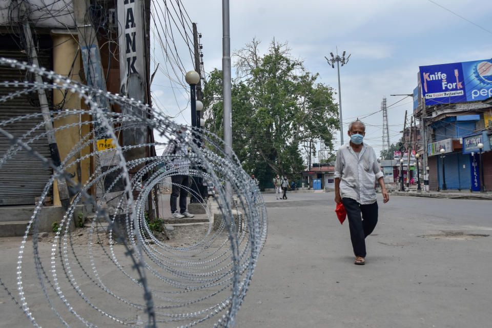 A man wearing a protective face mask walks past a concertina barricade erected by the government forces during a lockdown re-imposed to prevent the spread of coronavirus.Lockdown was re-imposed in Kashmir valley after a sudden surge in COVID-19 cases over the past one week, officials said Strict restrictions have been imposed and no movement of people, except for essential services and medical emergencies, are being allowed. (Photo by Saqib Majeed/SOPA Images/LightRocket via Getty Images)