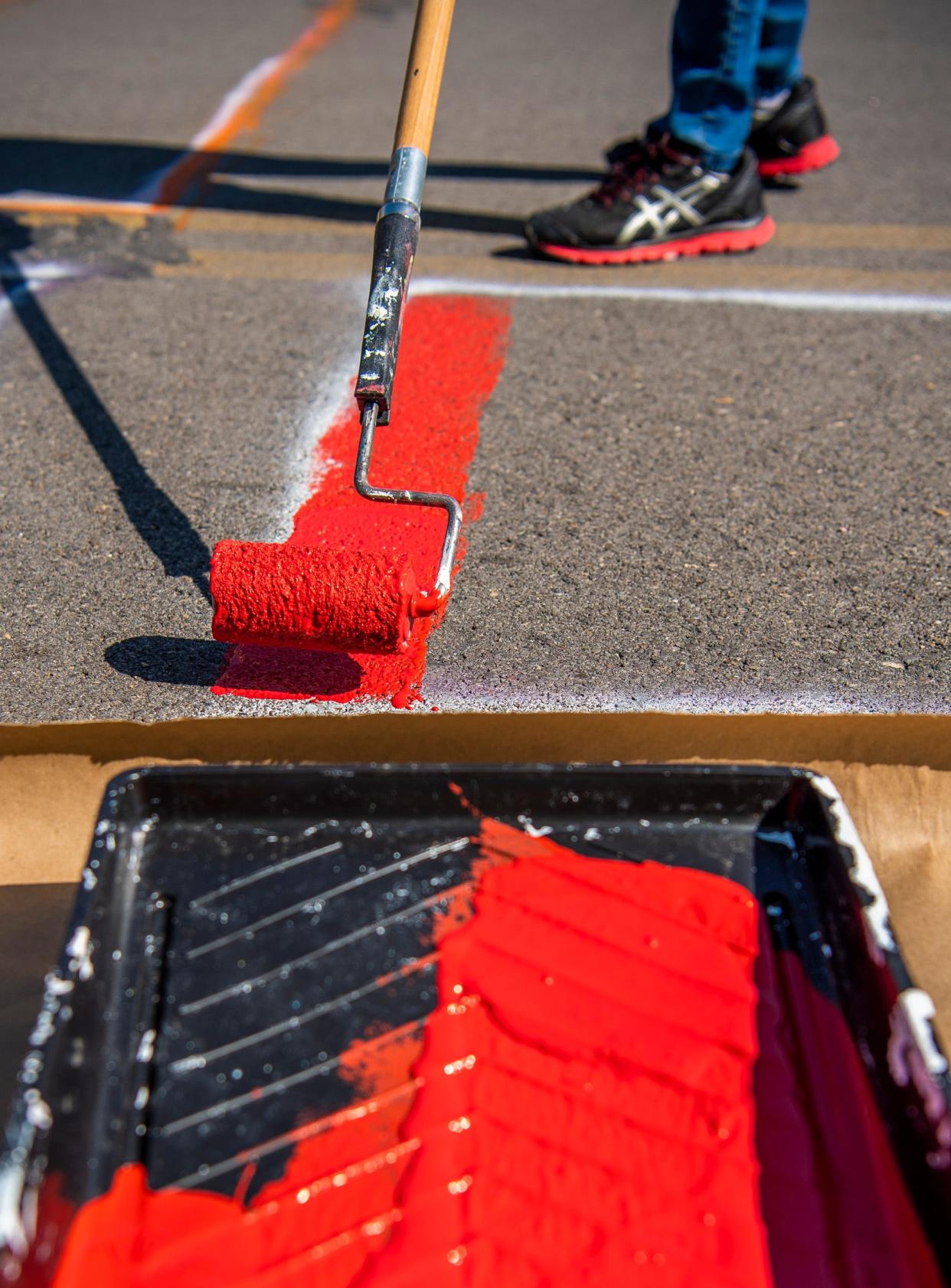 An activist rolls red paint onto Sixth Street in spring 2021 for the Black Lives Matter mural on the north side of the downtown square.