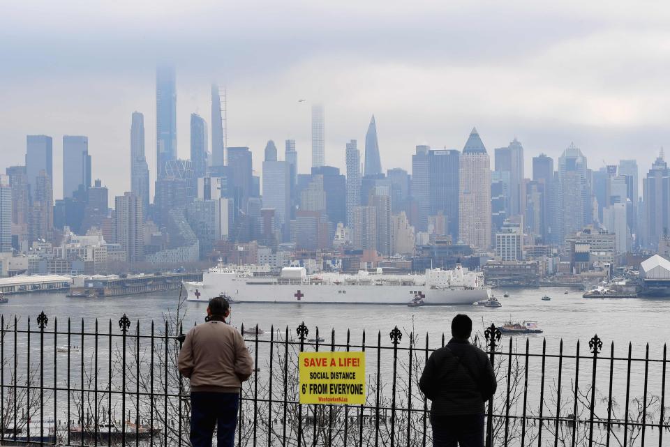 People watch as the USNS Comfort medical ship moves up the Hudson River as it arrives on March 30, 2020 in New York as seen from Weehawken, New Jersey.