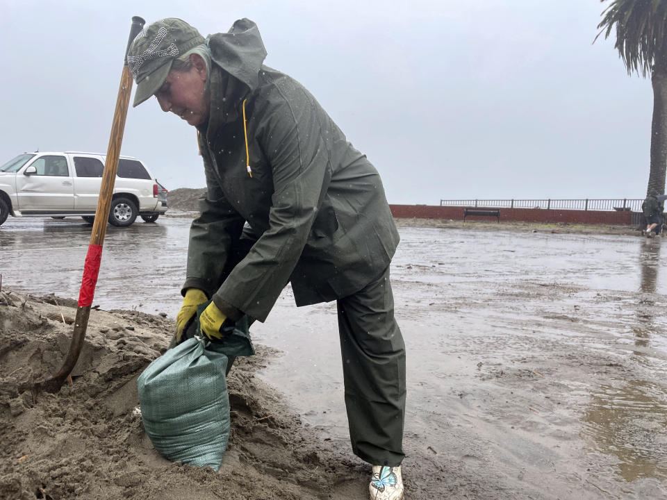 Resident Laurie Morse, 59, shovels wet sand into bags in the pouring rain, a last ditch effort to keep a rising creek out of her garage in the town of Rio Del Mar in Aptos, Calif., Wednesday, Jan. 11, 2023. Her roof was leaking, and along with her neighbors. The town has been dealing with every problem brought by the series of rainstorms rolling through California: massive logs and stumps are tumbling down the bloated Aptos Creek from the Santa Cruz mountains into the Monterey Bay, where high tides and large swells are tossing them back up the beach and into town. (AP Photo/Martha Mendoza)