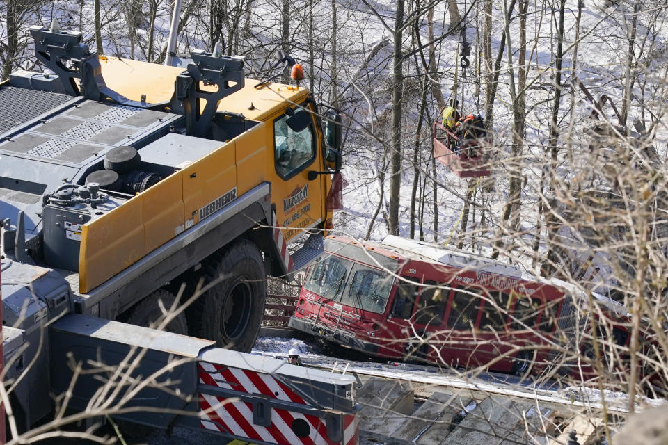 Workers in a basket suspended by a crane help with the recovery process on Monday Jan. 31, 2022 of the bus and other vehicles that were on a bridge when it collapsed Friday, in Pittsburgh's East End. (AP Photo/Gene J. Puskar)