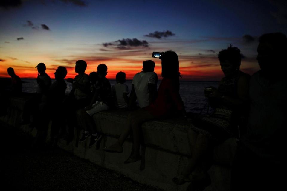People using their phones to snap images of the sunset at the seafront in Havana, Cuba (REUTERS)