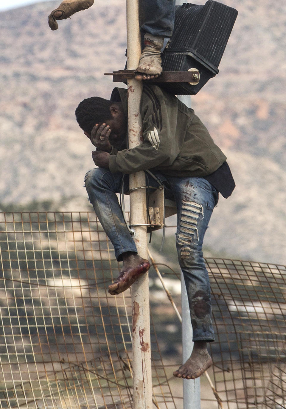 A sub-Saharan migrant sits on top of a pole set in a metallic fence that divides Morocco and the Spanish enclave of Melilla on Thursday April 3, 2014. Spanish and Moroccan police have thwarted a fresh attempt by dozens of African migrants to try to scale border fences to enter the Spanish enclave of Melilla. Thousands of sub-Saharan migrants seeking a better life in Europe are living illegally in Morocco and regularly try to enter Melilla in the hope of later making it to mainland Spain. (AP Photo / Santi Palacios)