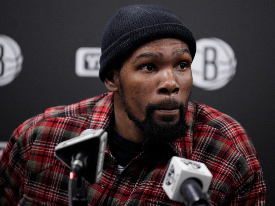 Kevin Durant leans in and raises his eyebrows while listening to a question at a press conference.