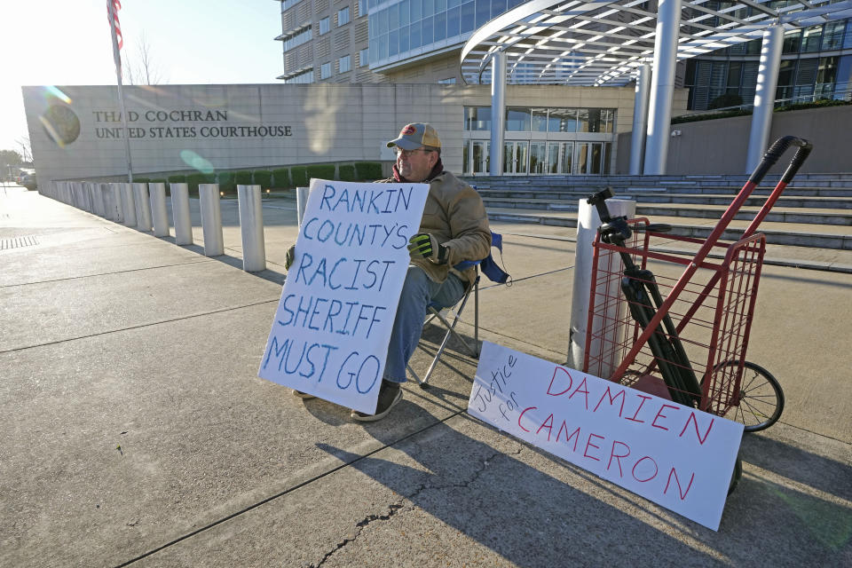 John Osborne, 62, of Jackson, sits outside the Thad Cochran United States Courthouse in Jackson, Miss., Tuesday, March 19, 2024, with signs of support for the two men abused by then six Mississippi Rankin County law enforcement officers who committed numerous acts of racially motivated, violent torture on Michael Corey Jenkins and his friend Eddie Terrell Parker in 2023. The six former law officers pleaded guilty to a number of charges for torturing them and their sentencing begins Tuesday in federal court. (AP Photo/Rogelio V. Solis)