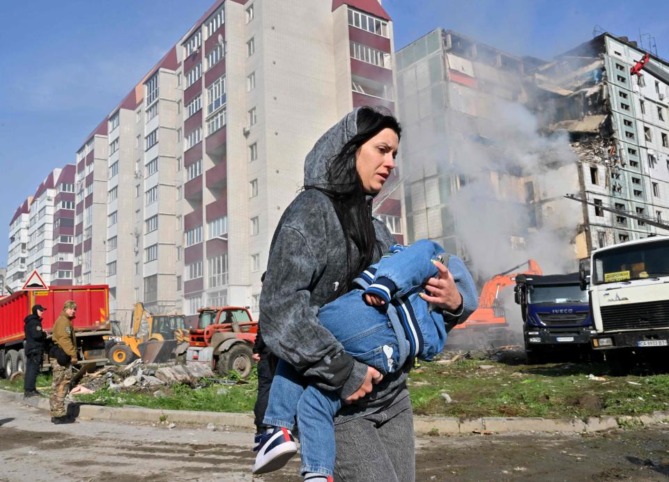 A woman walks past damaged residential buildings as she carries a child in Uman, around 215km southern Kyiv, on April 28, 2023, after Russian missile strikes targeted several Ukrainian cities overnight.