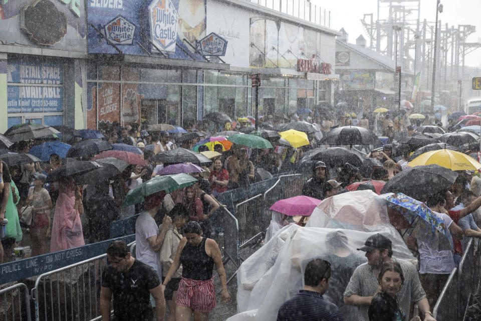 Una multitud se guarece de la lluvia luego de que el concurso anual de comer hot dogs organizado por Nathan's se suspendió brevemente debido a la tormenta, el martes 4 de julio de 2023, en Coney Island, Nueva York. (AP Foto/Yuki Iwamura)