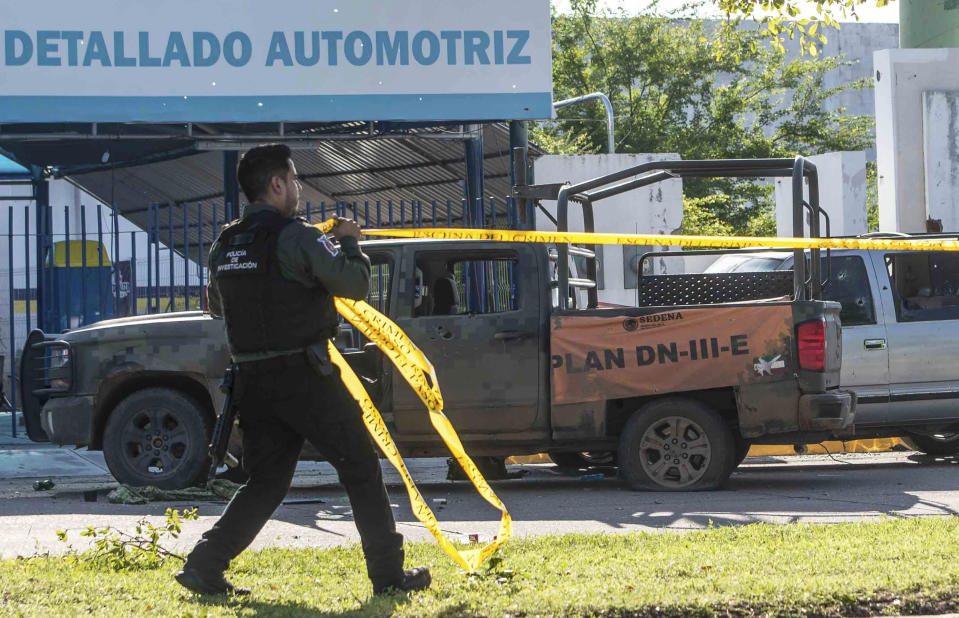 A Mexican police officer deploys tape to secure the scene around a bullet riddled armed forces truck, a day after gunmen and members of Mexico security forces clashed in a large gun battle in Culiacan, Mexico, Friday Oct. 18, 2019. Mexican security forces backed off an attempt to capture a son of imprisoned drug lord Joaquin "El Chapo" Guzman after finding themselves outgunned in a ferocious shootout with cartel enforcers that left at least eight people dead and more than 20 wounded, authorities said Friday. (AP Photo/Augusto Zurita)