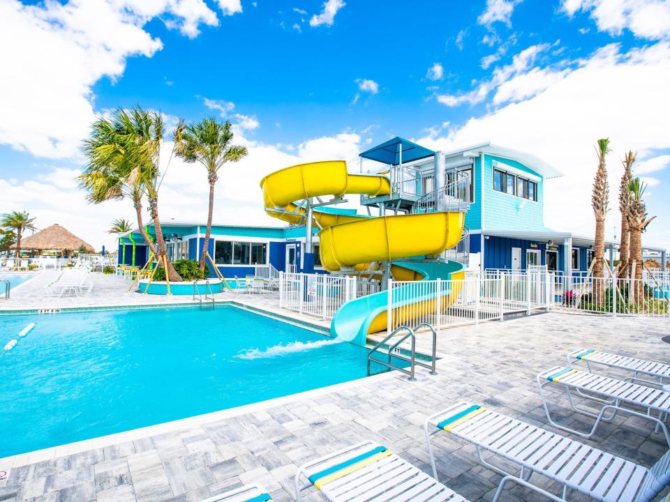 An empty pool with lounge chairs and a water slide. It's a bright blue day with clouds.