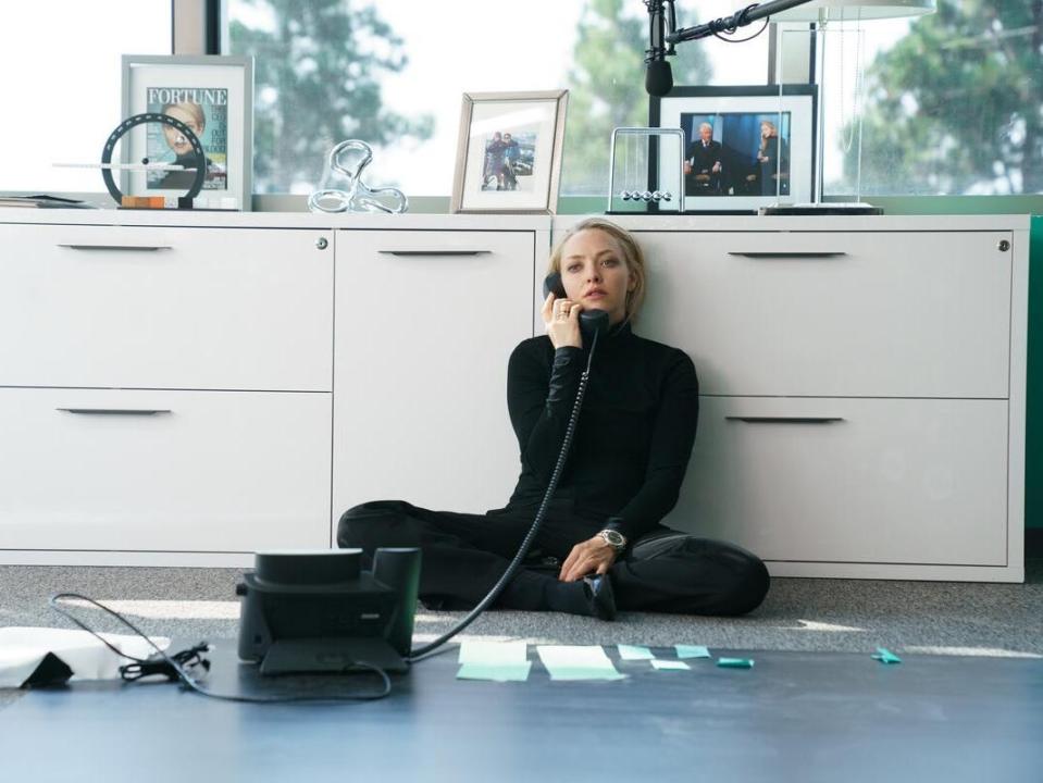 Amanda Seyfried dressed in black on the phone sitting on the floor