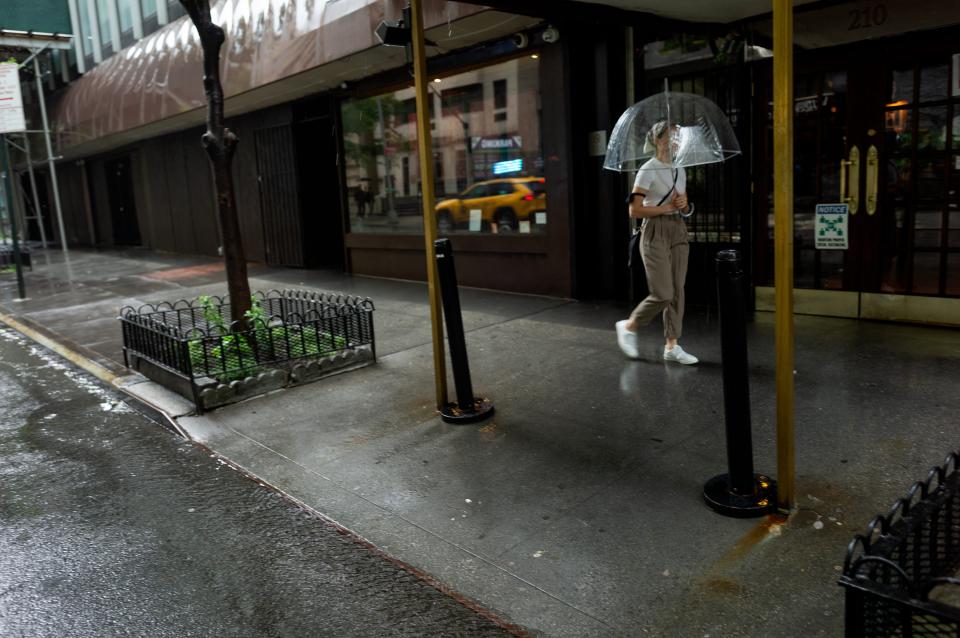 A view of a sidewalk with a woman, holding an umbrella, walking by.