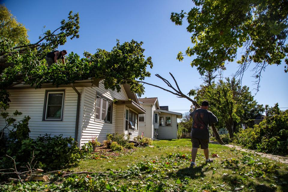 Bruce Rook uses a chainsaw to cut a tree that fell on Jerry Eash's house home in Marshalltown as Eash moves limbs to the curb Tuesday, Aug. 11, 2020. A derecho packing winds from 80 to 100 mph stormed through Iowa the day before.