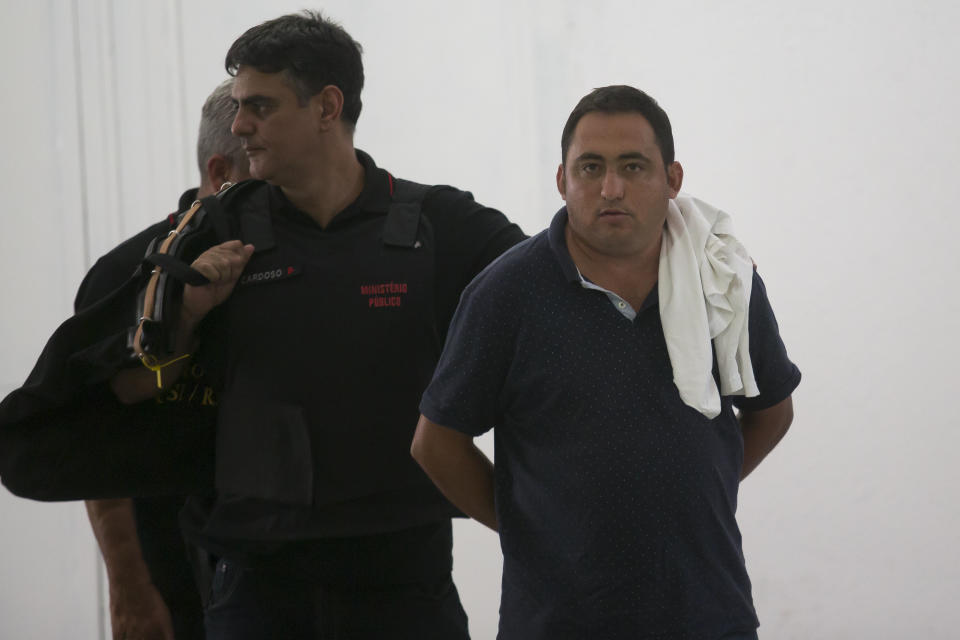 Manuel de Brito Batista, right, member of a militia gang, is detained by the police in Rio de Janeiro, Brazil, Tuesday, Jan. 22, 2019. Rio civil police and public prosecutors are booking five leaders of a militia gang into prison for extortion, illegal land occupation, bribery to public agents, and illegally carrying firearms, among other things. (AP Photo/Bruna Prado)