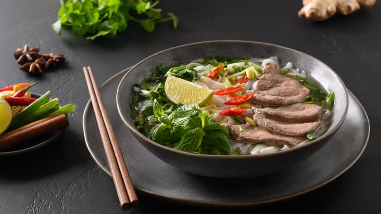 Pho soup with beef in bowl with herbs, spices, and chilis