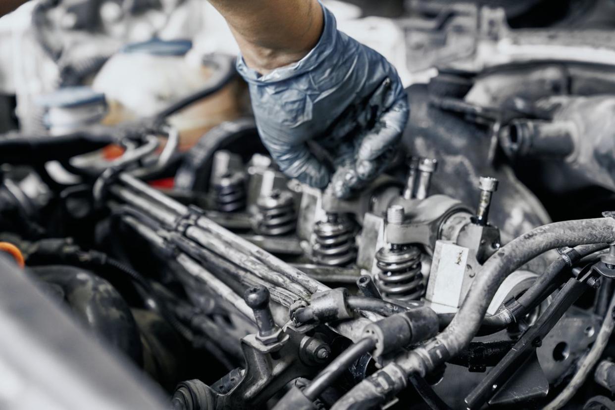 Close up of nozzles in car diesel engine with mechanic's hand in blue dirty rubber gloves doing professional auto repairing. Engine maintenance concept