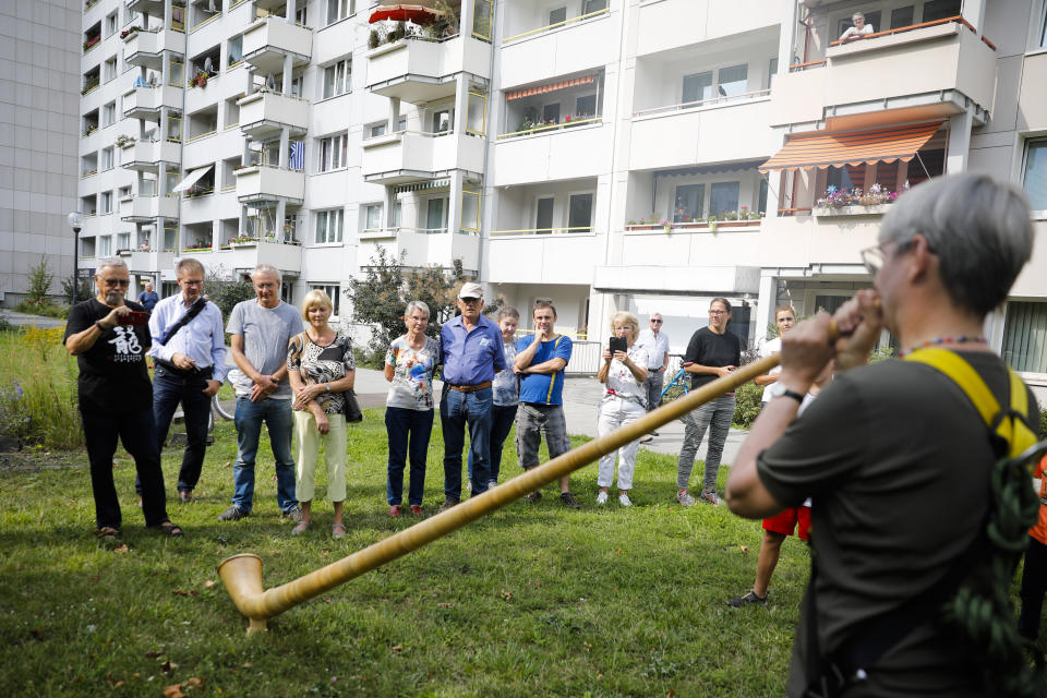 Spectators listen to a musician with an alphorn walk between residence buildings during the 'Himmel ueber Prohils', Sky over Prohlis, concert event at the Prohlis neighbourhood in Dresden, Germany, Saturday, Sept. 12, 2020. About 33 musicians of the Dresden Sinfoniker perform a concert on the rooftops of the Dresden neighbourhood Prohlis. (AP Photo/Markus Schreiber)