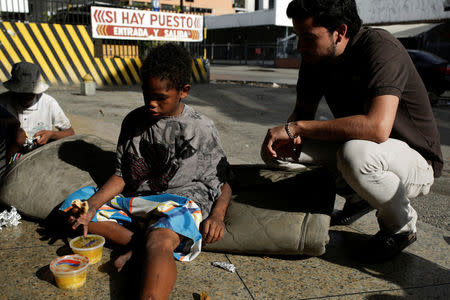 A volunteer of Make The Difference (Haz La Diferencia) charity initiative speaks with a homeless child after giving him a cup of soup and an arepa in a street of Caracas, Venezuela March 5, 2017. REUTERS/Marco Bello