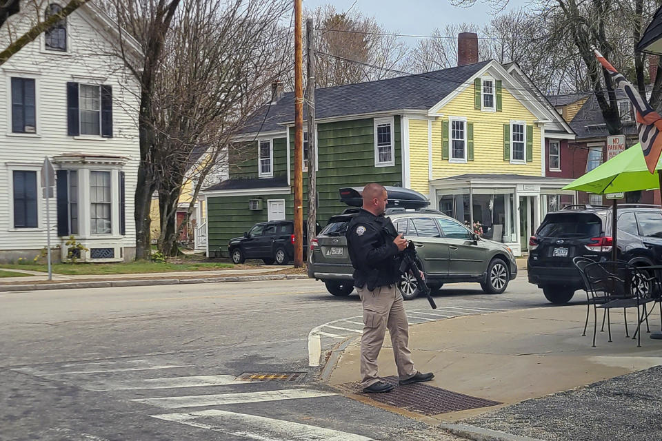 A police officer stands on the corner of Portland Street and Main Street in Yarmouth, Maine, on Tuesday, April 18, 2023. State police say gunfire that erupted on a busy highway is linked to a second crime scene where several people were found dead in a home about 25 miles away in the town of Bowdoin, Maine. Police briefly ordered people in nearby neighborhoods to shelter in place, but authorities later announced there was no threat to the public. (Michael Leonard via AP)