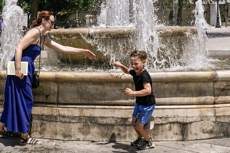 Una madre se refresca del calor con su hijo jugando con agua alrededor de una fuente en Atenas el 20 de julio de 2023. 