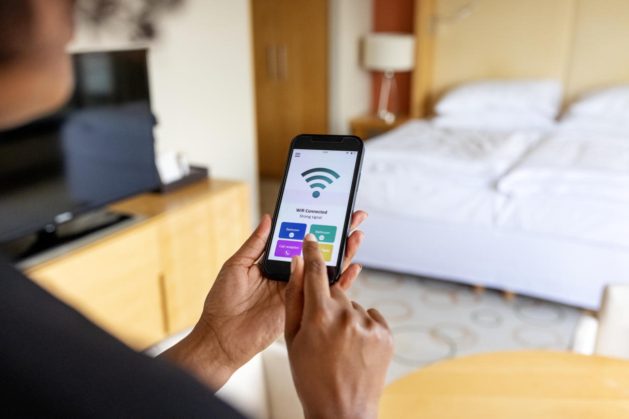 Over the shoulder view of businesswoman connecting to the mobile wifi in hotel room. Wifi icon on mobile phone display.