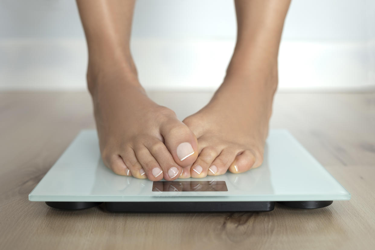 Ashamed feets of a barefoot female on weighing scale.