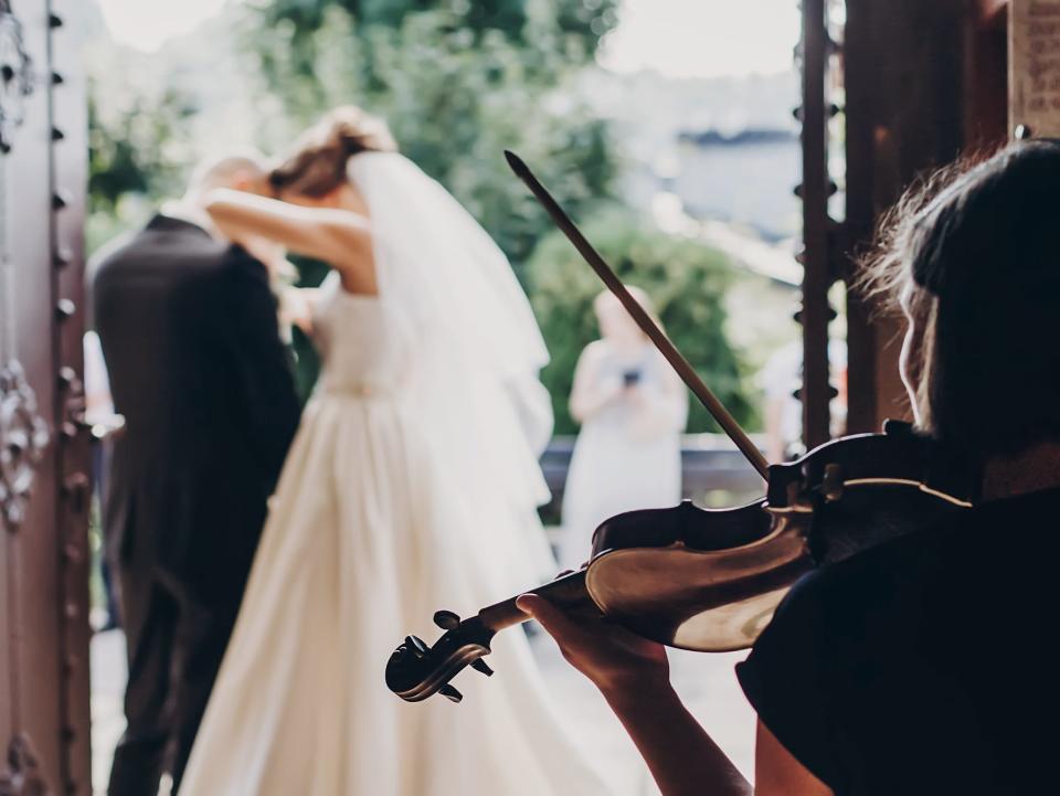 person playing violin at a wedding with a married couple in the background